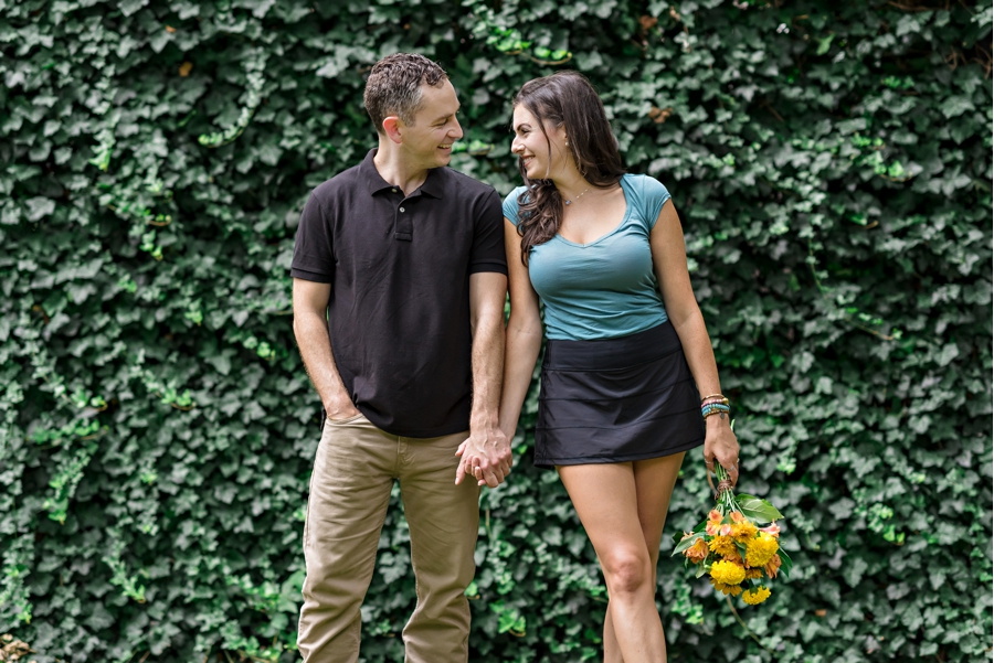 A cute couple stand in front of an ivy wall in Rittenhouse Square.